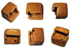 DEJ-4018 - Dé pipé (os)osDé massif dont une partie du volume intérieur a été évidé et rempli de plomb, en utilisant les cercles oculés des faces adjacentes pour creuser un vide à l'aide d'outils miniaturisés, avant de combler le vide par du plomb et de reboucher les orifices avec des opercules en os.