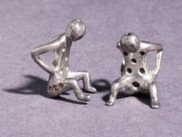 DEJ-9005 - Dé en forme de personnage accroupiargentDé en forme de figurine assise, les mains posées sur les hanches et les coudes ramenés en arrière. Le chiffrage comprend 6 points sur le torse et d'autres sur le dos ; les points creux sont soulignés de rouge.