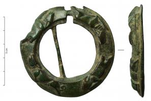 FER-7015 - Fermail à reliefsbronzeBoucle épaisse, coulée, avec une bordure oblique ornée de reliefs figurés (chiens courant); une encoche est prévue pour l'articulation d'un ardillon, et une fine barre transversale a été coulée en travers de l'ouverture, mais en position oblique.