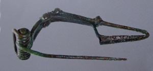 FIB-3956 - Fibule de type KastavbronzeTPQ : -200 - TAQ : -50Fibule de schéma La Tène II, coulée, avec un ressort de longueur moyenne dont la corde s'enroule autour de la tête de l'arc. le pied replié et orné de boutons est rattaché à l'arc par une bague (une variante est coulée d'un seul tenant).