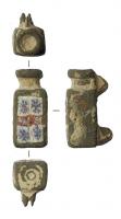 FIB-41547 - Fibule skeuomorphe : bouteillebronzeFibule en forme de bouteille carrée, à corps étranglé, avec sous le fond les cercles concentriques qui indiquent un vase en verre moulé; sur le côté externe, décor d'émaux millefiori.