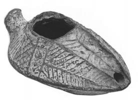 LMP-41506 - Lampe pantoufle byzantine terre cuiteLampe allongée à bec incorporé à canal décoré d'une feuille de palme; épaule décorée de traits et de motifs géométriques en relief. Petite anse en forme de louche.