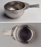 PAT-4085 - Patère à manche en queue d'arondeargentCasserole à panse basse et trapue, profil arqué, lèvre en bourrelet vers l'extérieur ; panse lisse ou marquée de godrons ; le fond est travaillé de façon à dégager sur le pourtour un anneau plat formant pied. Le manche massif, est plat, à côtés concaves, avec une extrémité libre découpée en queue d'aronde ; vers la vasque, découpe en une succession de volutes pouvant évoquer des têtes d'oiseaux.